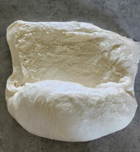 sourdough bread dough being rolled and shaped into a loaf