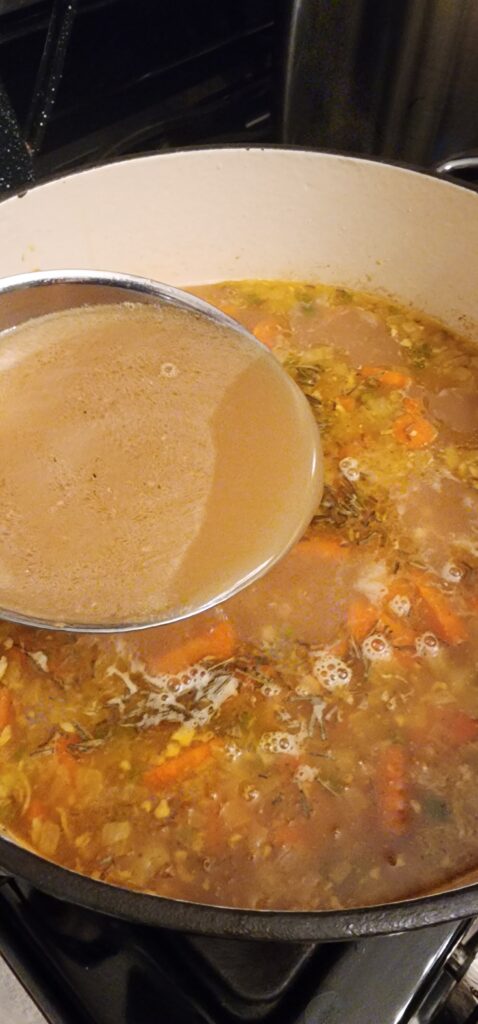 ladle of chicken broth over pot of chicken soup