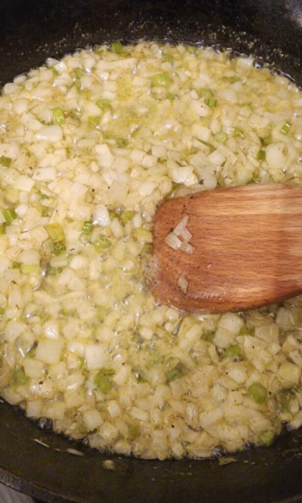 skillet cooking onions and celery with wooden spoon